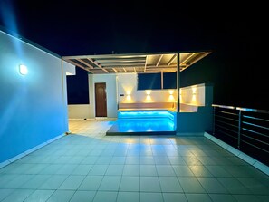 Un área de piscina en la azotea con cerramiento de vidrio, una puerta e iluminación en la pared.