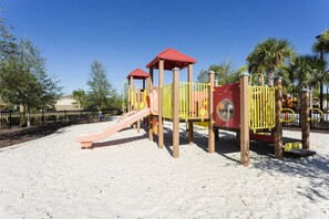 A sandy playground with a slide and climbing structures.