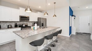 A modern kitchen with white cabinets, a granite countertop, stainless steel appliances, and three bar stools.