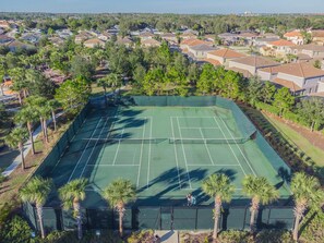An aerial view of a tennis court surrounded by residential houses and palm trees.