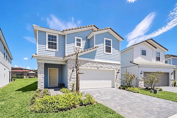 A two-story house with a stone facade, a garage, and a well-maintained lawn. - Family Luxury 7BR Pool Home at Solterra (Davenport)