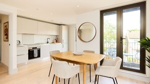 A modern kitchen with white cabinets, a wooden dining table, and four white chairs. - The South Wimbledon Hideout - Fancy 1bdr Flat With Balcony (London)