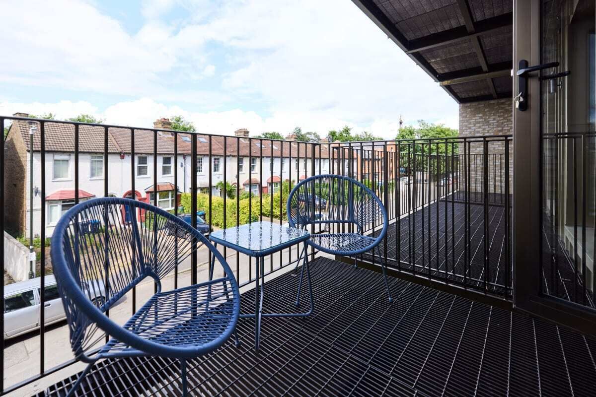 A balcony with two blue metal chairs and a small table.