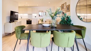 A modern dining area with a dark wooden table, green upholstered chairs, and a vase with flowers. - The South Wimbledon Escape - Lovely 3bdr With Balcony (London)