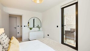 A bedroom with a bed, a dresser, a mirror, and a sliding glass door to a balcony. - The South Wimbledon Escape - Lovely 3bdr With Balcony (London)