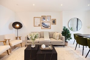 A modern living room with a sofa, coffee table, and a dining area with chairs. There are framed pictures on the wall and a potted plant. - The South Wimbledon Escape - Lovely 3bdr With Balcony (London)
