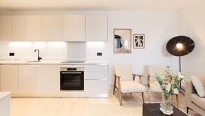 A modern kitchen with white cabinetry, a built-in oven, and a dining area with a sofa and chairs. - The South Wimbledon Escape - Lovely 3bdr With Balcony (London)