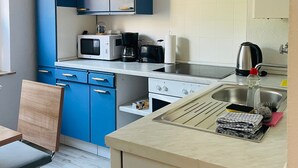 A compact kitchen with blue cabinets, a microwave, a kettle, and a sink.