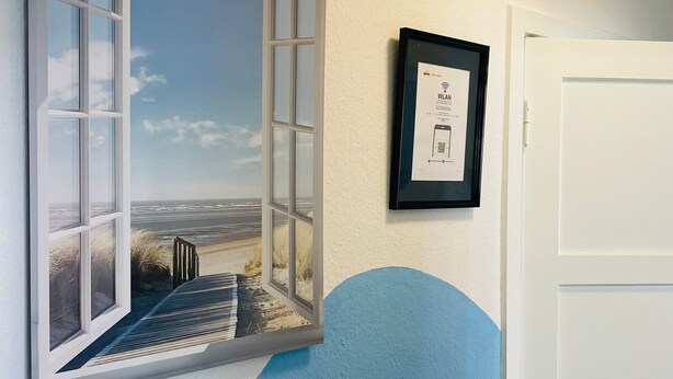 A room with a large window overlooking a beach, a framed picture on the wall, and a white door.
