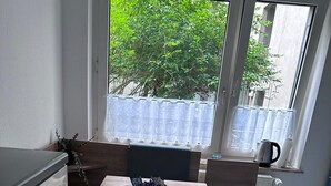 A modern kitchen with a wooden table, two blue chairs, and a window with a view of greenery.