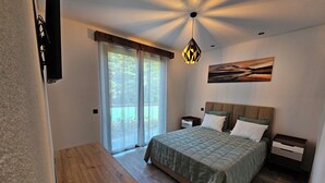 Ein Schlafzimmer mit einem Bett, einem Nachttisch, einer hölzernen Bank, einer Deckenleuchte und einem Fenster mit Vorhängen.