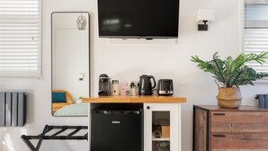 Et lille tekøkken med køleskab, kaffemaskine, elkedel og en potteplante.