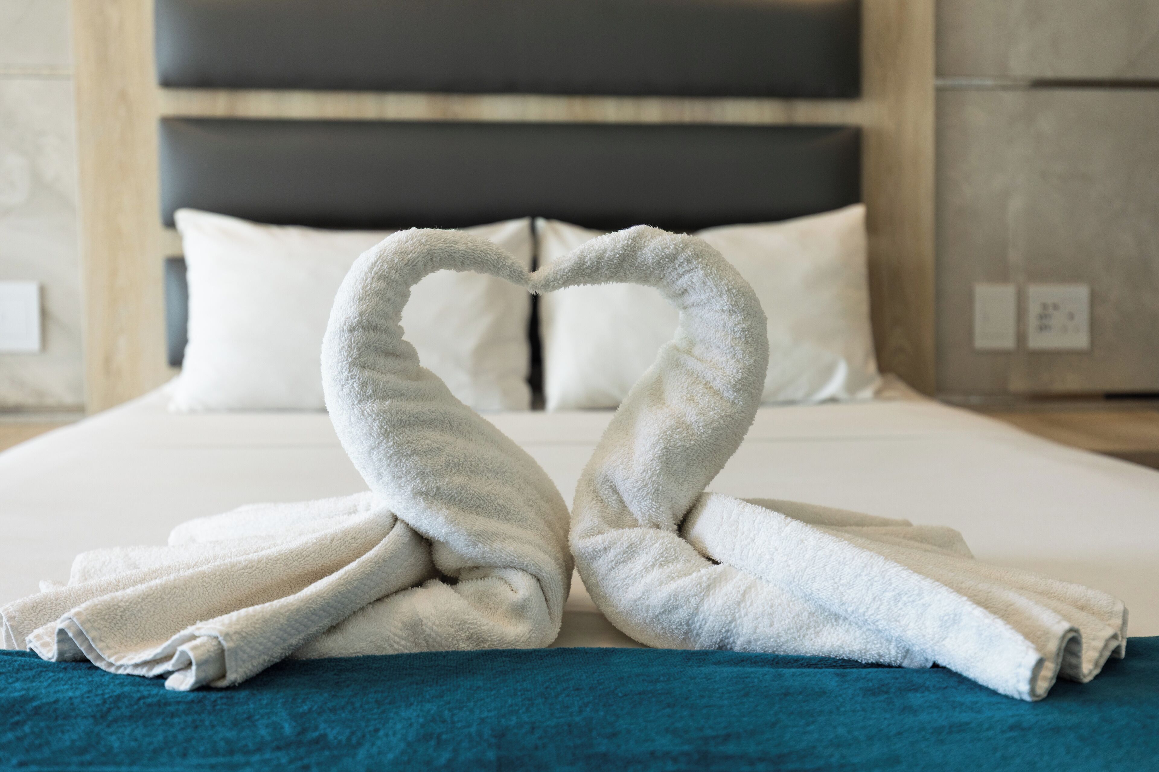 Una cama con una toalla dispuesta en forma de corazón sobre una manta azul.