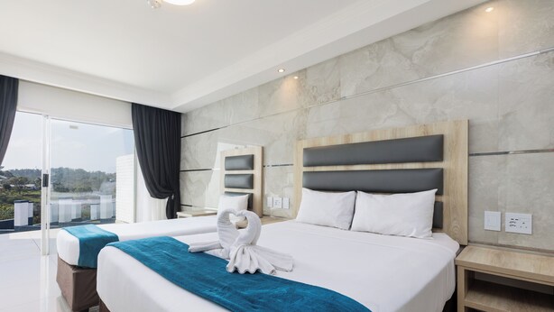 Habitación de hotel moderna con una cama grande, un sofá cama independiente, un balcón con cortinas y vistas al paisaje.