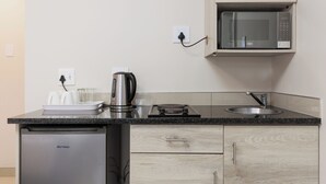 A compact kitchen with a microwave, kettle, and a small sink. - Bayside Taj Hotel (Port Shepstone)