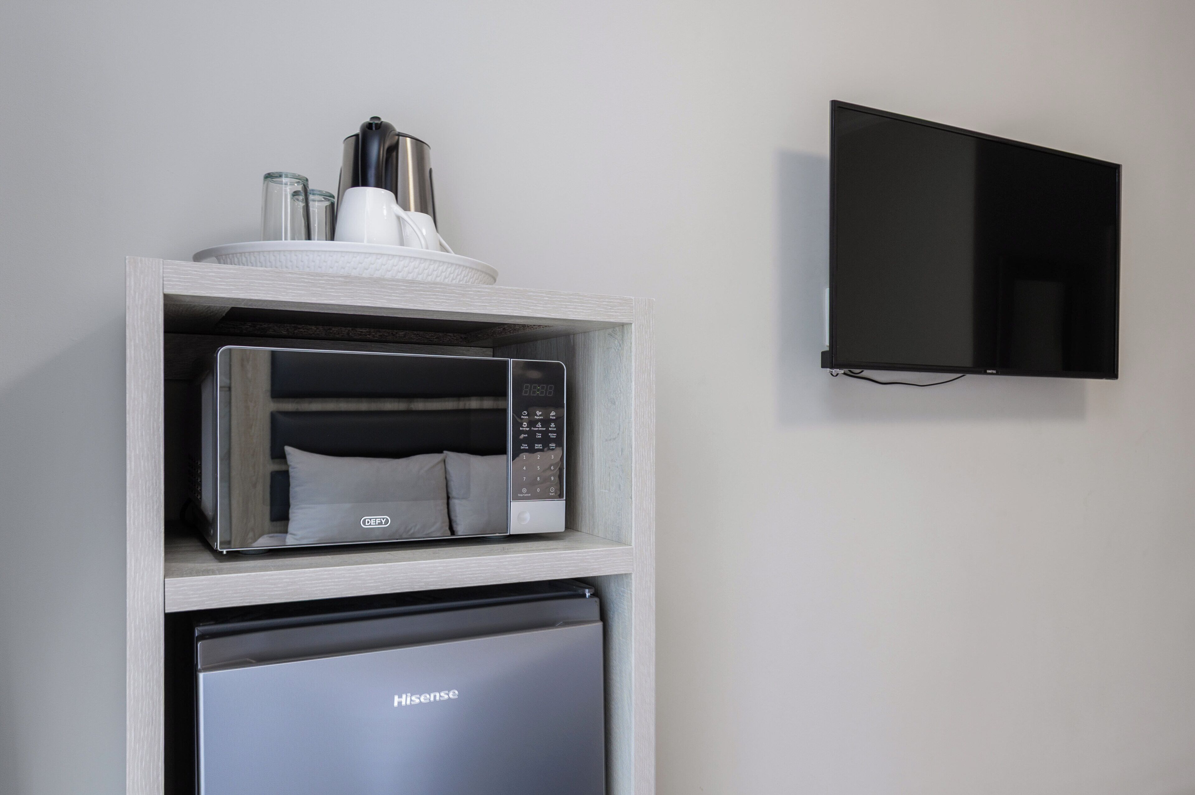 Una cocina con microondas y refrigerador, ambos con la etiqueta 'Hisense', y un televisor de pantalla plana montado en la pared.