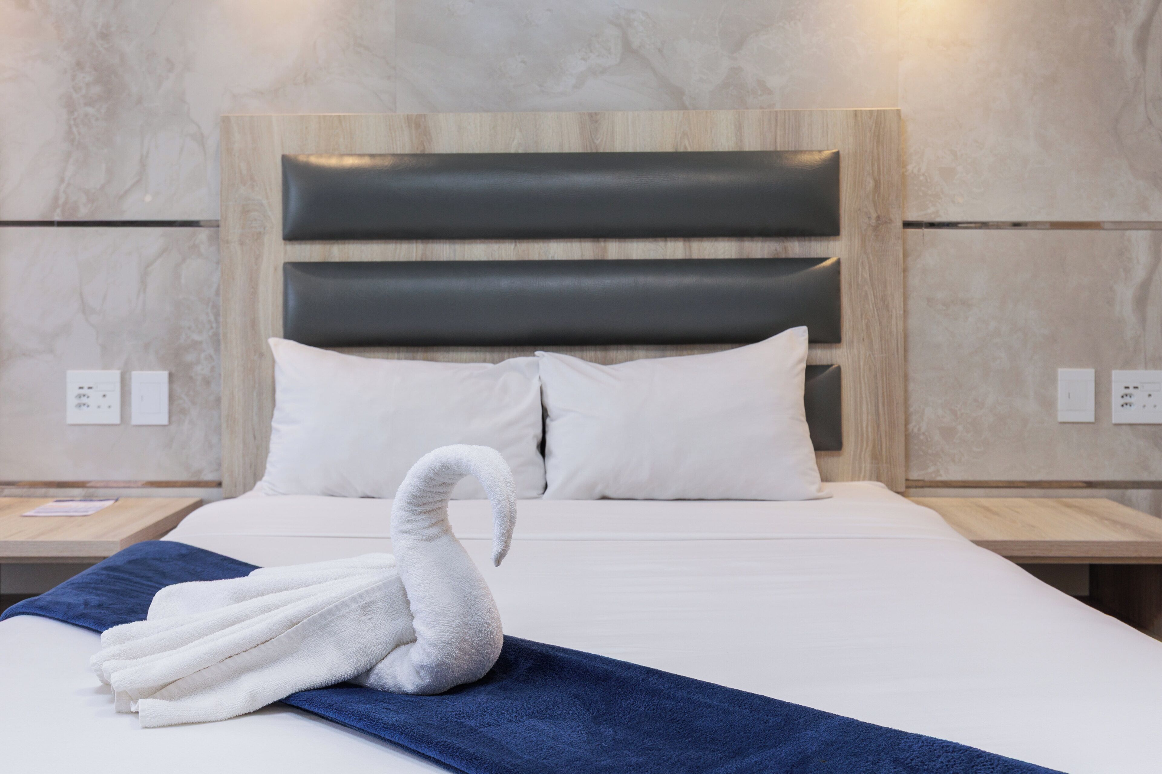 Habitación de hotel con una cama, cabecera y una decoración de toallas con forma de cisne.