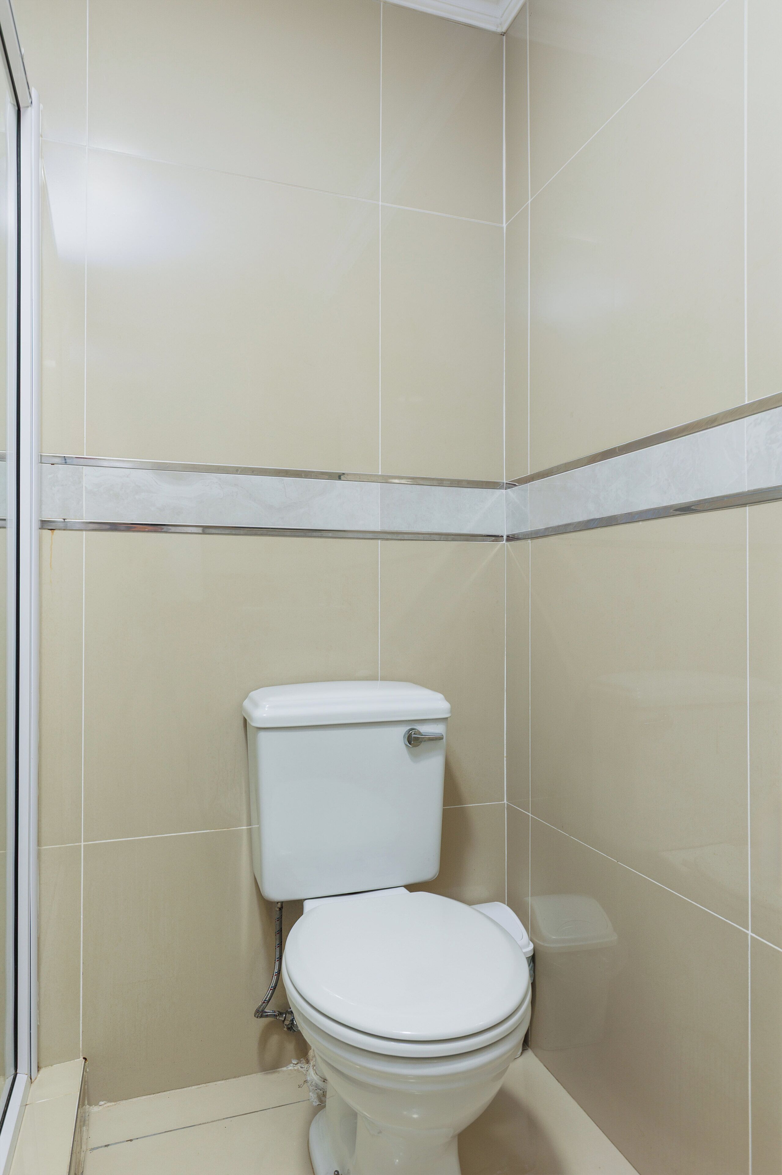 Un baño pequeño y cerrado con inodoro, un cubo de basura y zona de ducha.