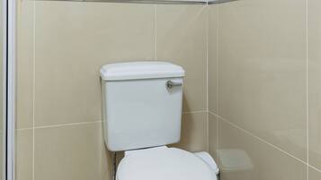 Un baño pequeño y cerrado con inodoro, un cubo de basura y zona de ducha.
