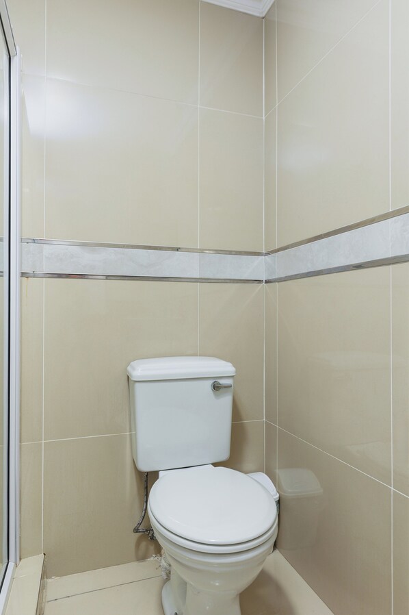 A small, enclosed bathroom with a toilet, a trash bin, and a shower area.