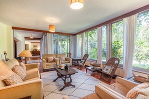 A spacious living room with a large window, a sofa set, a coffee table, and a wooden chair.