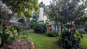 Um jardim exuberante com diversas plantas e um pequeno edifício com varanda.