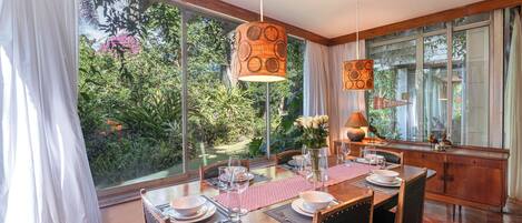 A dining area with a large window, wooden table, chairs, and a hanging light fixture.