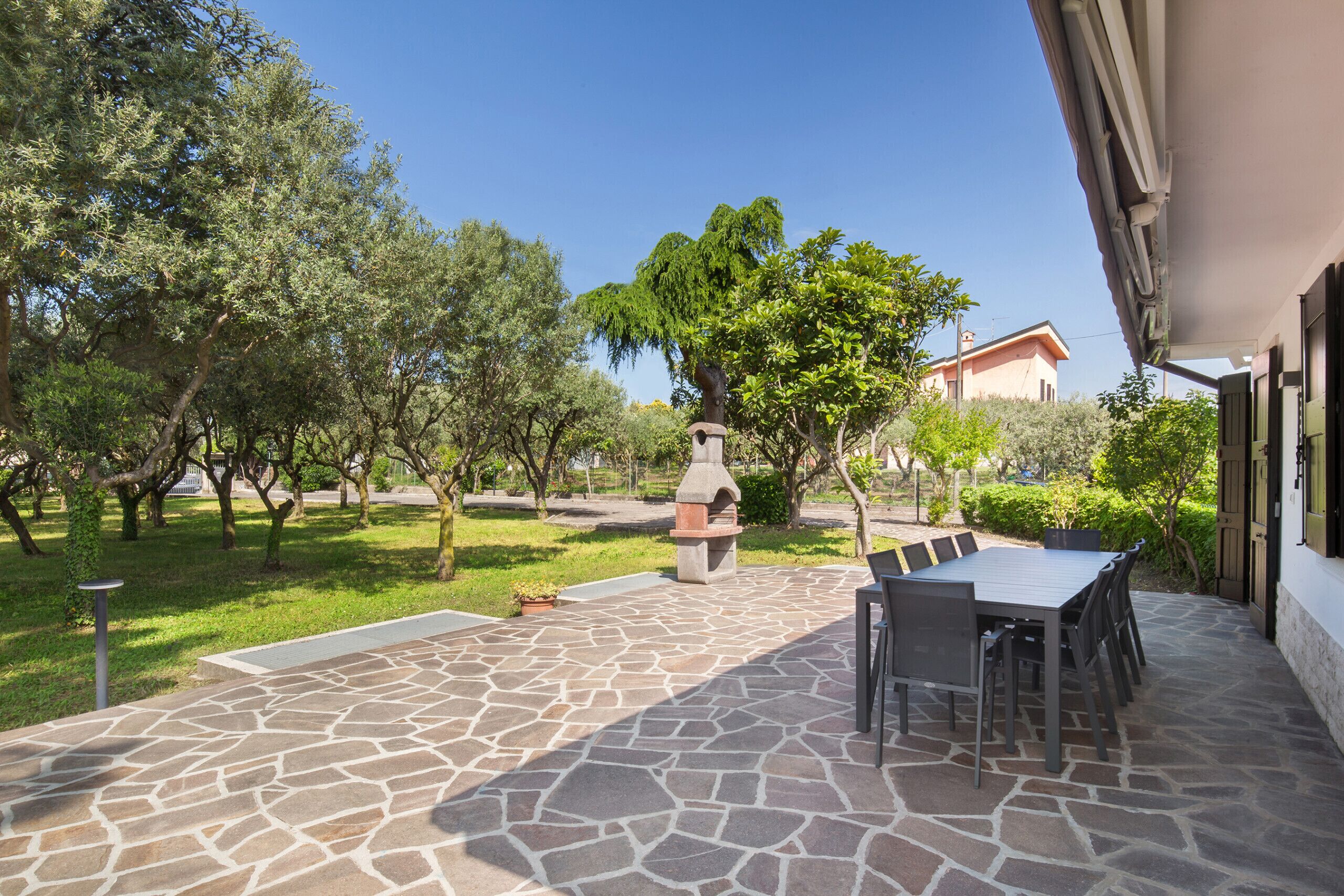 An outdoor patio with stone flooring, a grill, and a dining table with chairs.