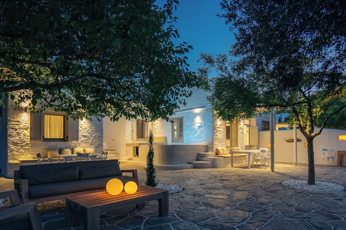 An outdoor patio area with stone flooring, wooden furniture, and ambient lighting.