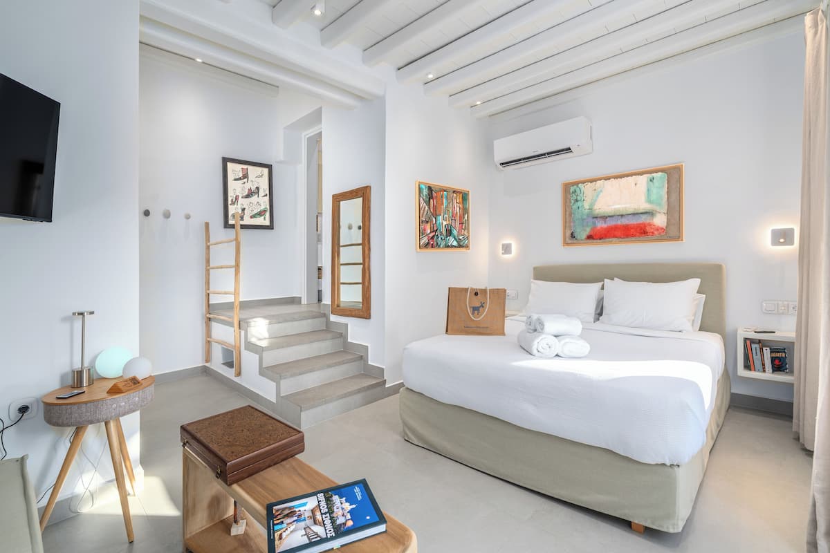 A modern hotel room with a large bed, a TV, a desk, and a staircase leading to another room.