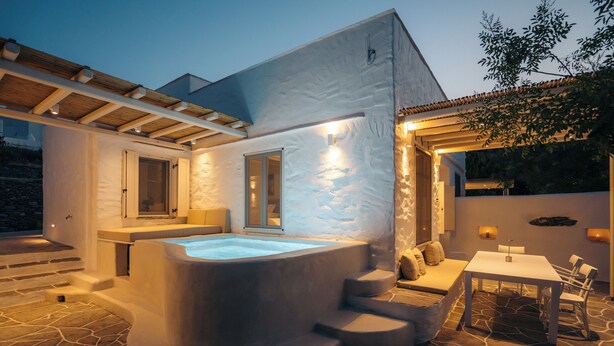 A modern outdoor hot tub area with stone flooring, a wooden pergola, and a seating area with a table and chairs. - Rabagas Suites (Sifnos)