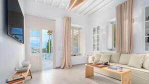 A modern living room with a sofa, coffee table, and a TV mounted on the wall. - Rabagas Suites (Sifnos)