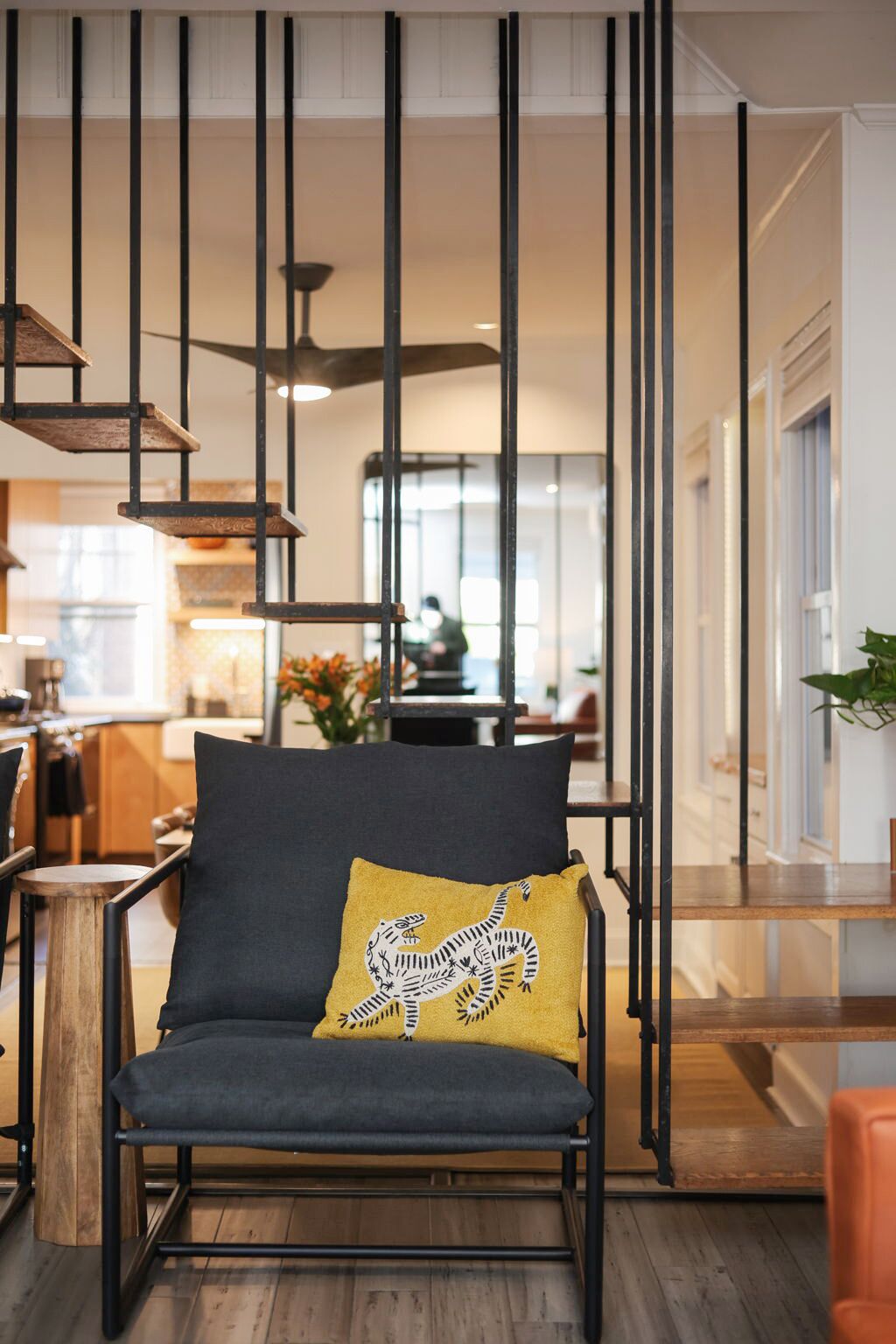 Uma sala de estar moderna com um sofá cinza escuro, uma almofada amarela com estampa de cobra e uma mesa de centro de madeira.