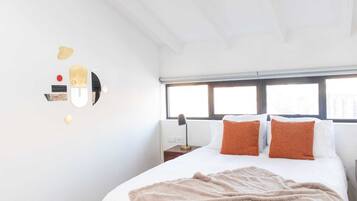 Un dormitorio con una cama grande, dos almohadas, una mesita de noche con una lámpara y una ventana con persianas.