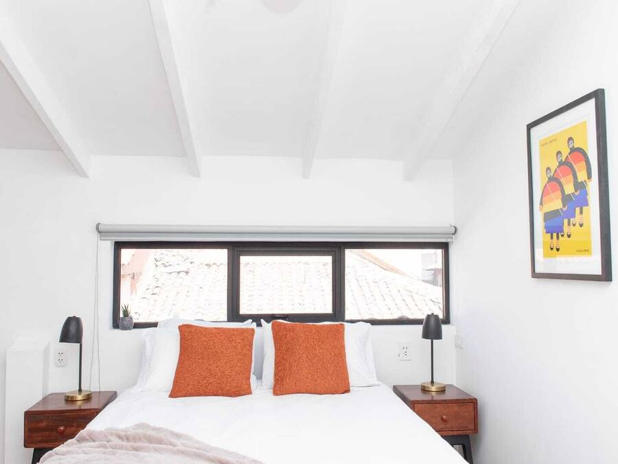 A bedroom with a bed, two nightstands, a window, and a framed picture on the wall.