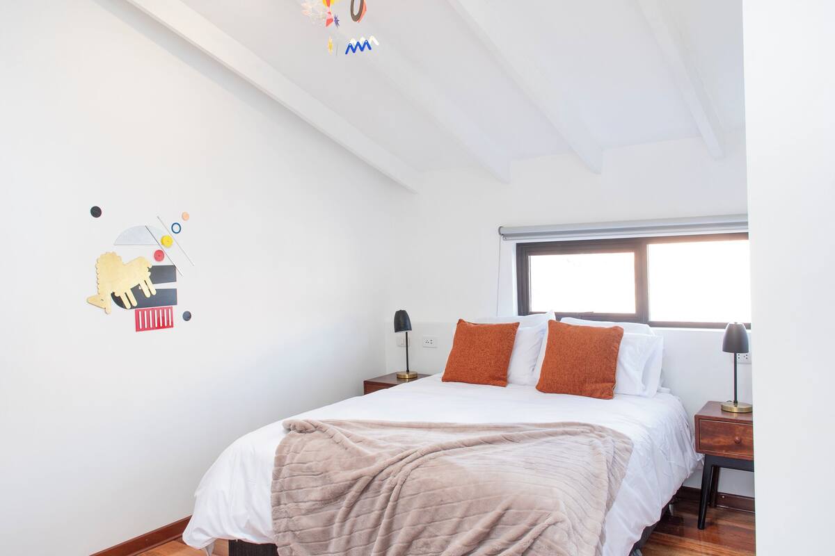 Un dormitorio con una cama, dos mesitas de noche, una ventana y un adorno en la pared.