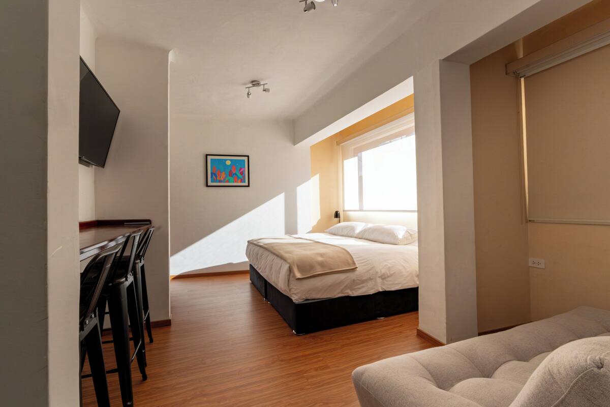 Un dormitorio con una cama, un escritorio, una silla, una ventana y un cuadro en la pared.