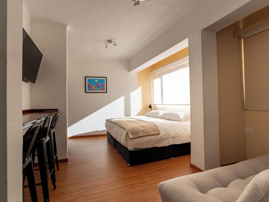 A bedroom with a bed, a desk, and a chair, a window, and a painting on the wall.