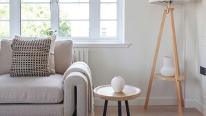 Un salon avec un canapé, une petite table ronde, un lampadaire et une fenêtre avec des stores.