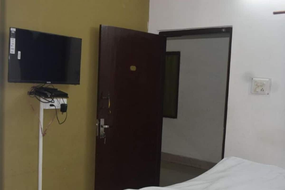 Una habitación de hotel con una cama, un televisor fijado a la pared y una puerta que da a otra habitación.
