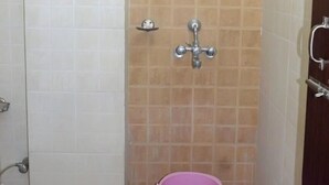 A small bathroom with a shower, a toilet, and a pink bucket. - Ali Baba Guest House (Varanasi)