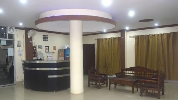 A reception area with a counter, two wooden benches, a pillar, and a large window with curtains. - Ali Baba Guest House (Varanasi)