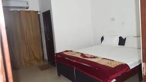 A room with a bed, a wooden headboard, a red bedspread, a white wall, and a door with a curtain. - Ali Baba Guest House (Varanasi)