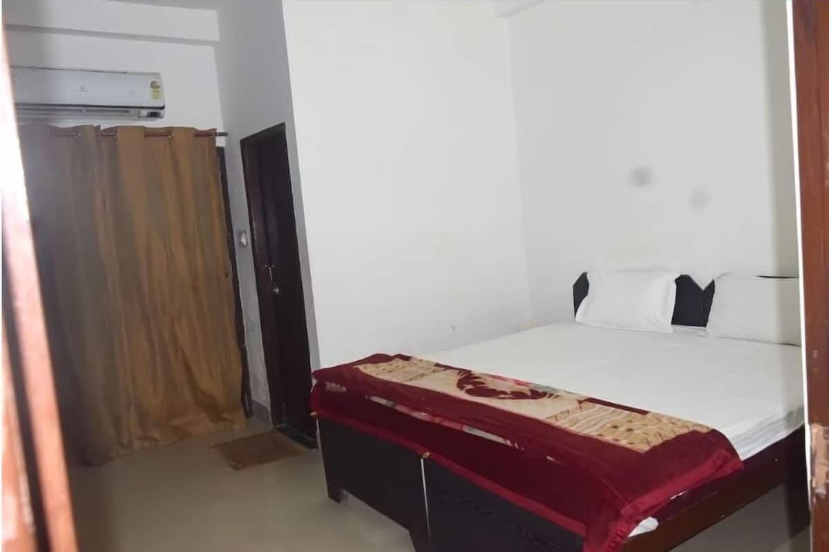 Una habitación con cama, cabecera de madera, colcha roja, pared blanca y una puerta con cortina.