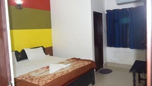 A room with a bed, a small table, an air conditioning unit, and a door. - Ali Baba Guest House (Varanasi)