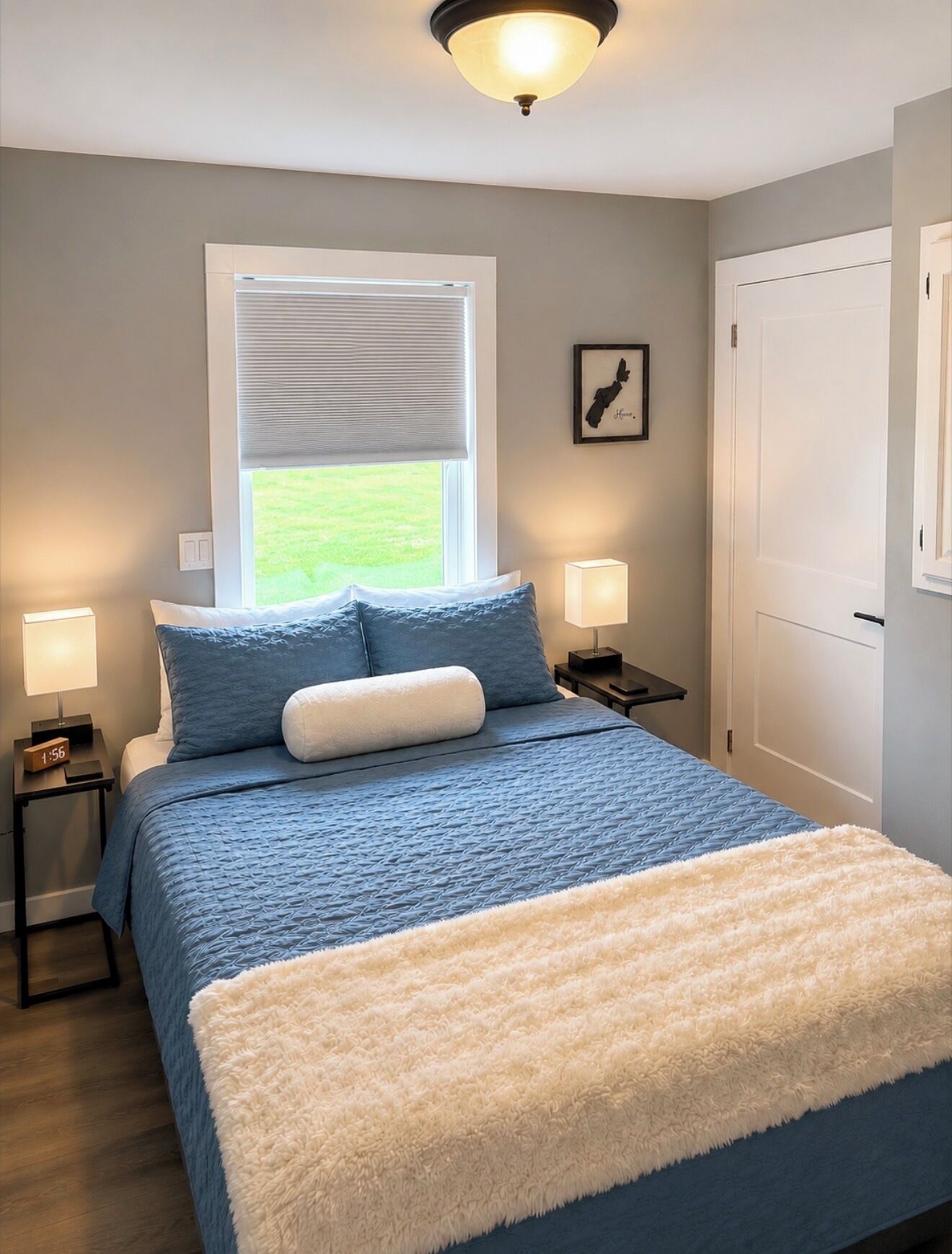Une chambre à coucher comprenant un lit, des lampes de chevet, une fenêtre avec des stores, une porte et un luminaire fixé au mur.