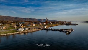 A waterfront town with a prominent church, calm water, and a dock with boats. - Nanook’s Den Escape to the beauty of the mountains               Internet, GBTV (Petit Étang Cheticamp)