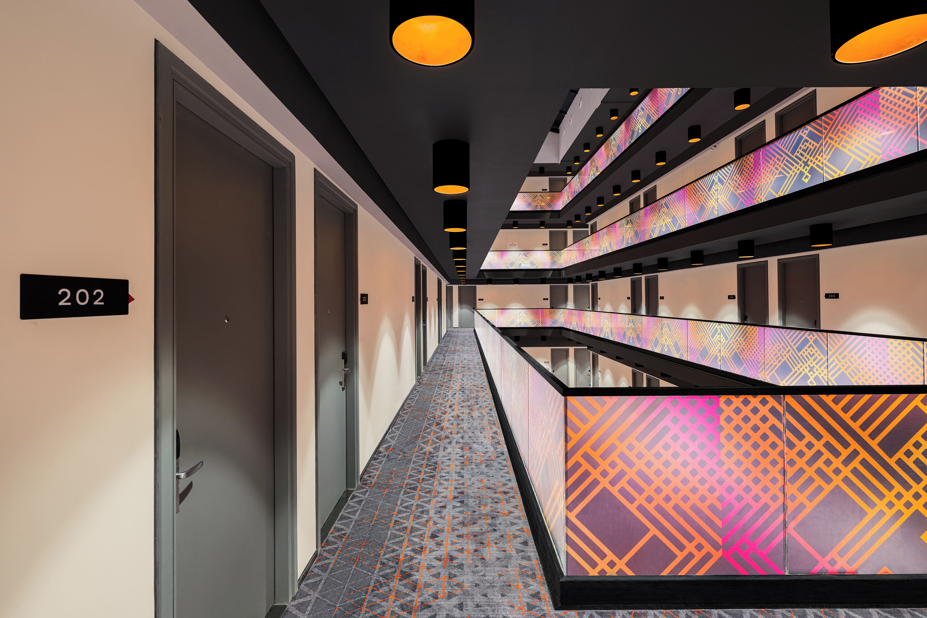 Pasillo de hotel con piso estampado, varias puertas y un cartel con el número de habitación 202.