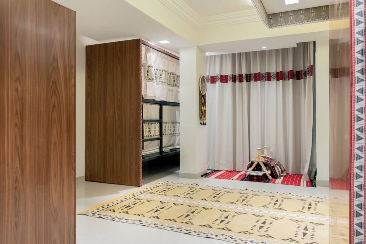 Una habitació amb un llit superposat, un armari de fusta, una catifa estampada i cortines amb un disseny vermell i blanc.