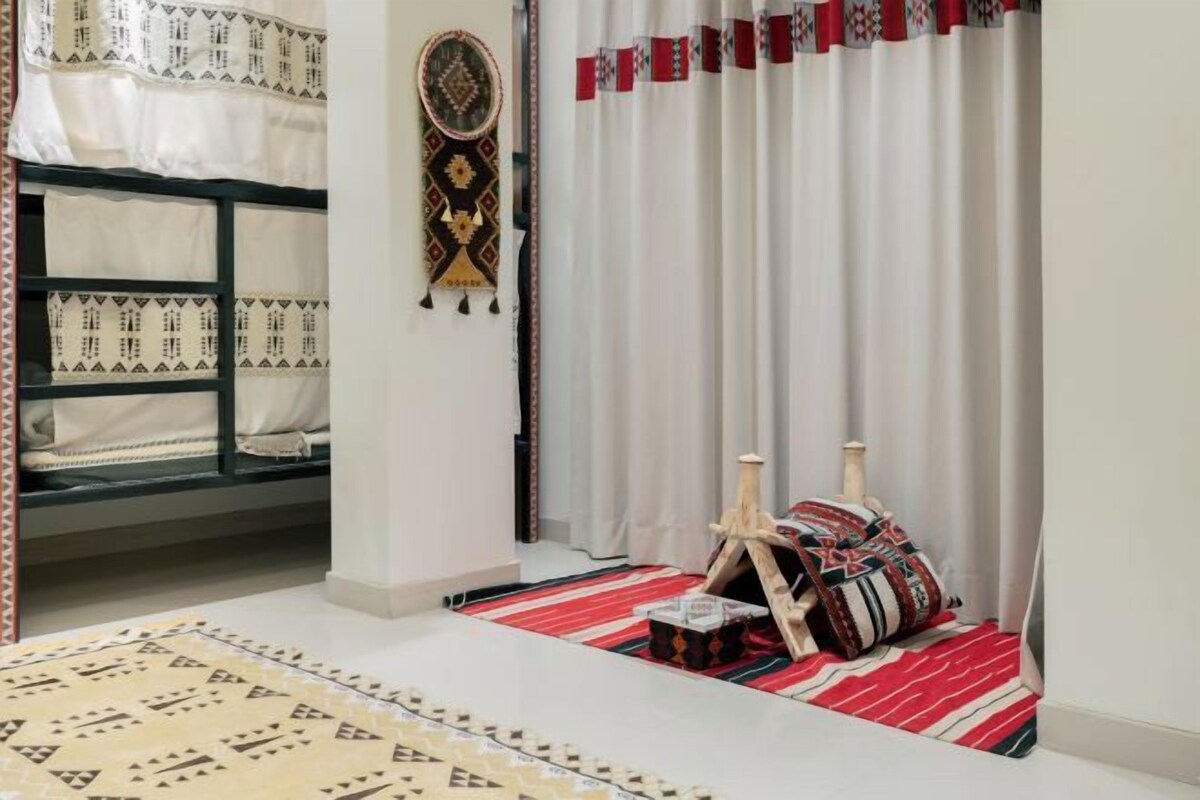 A room with a bunk bed, a patterned rug, a decorative wall hanging, and a curtain with a red and white pattern.